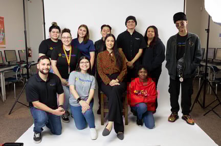 A group of staff and students posing together for a group photo in front of a white backdrop inside a classroom